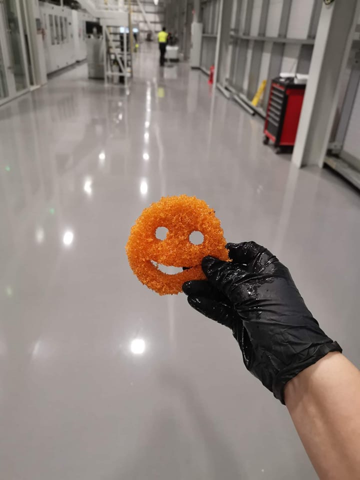 someone wearing a black rubber glove holding an orange smiley face sponge